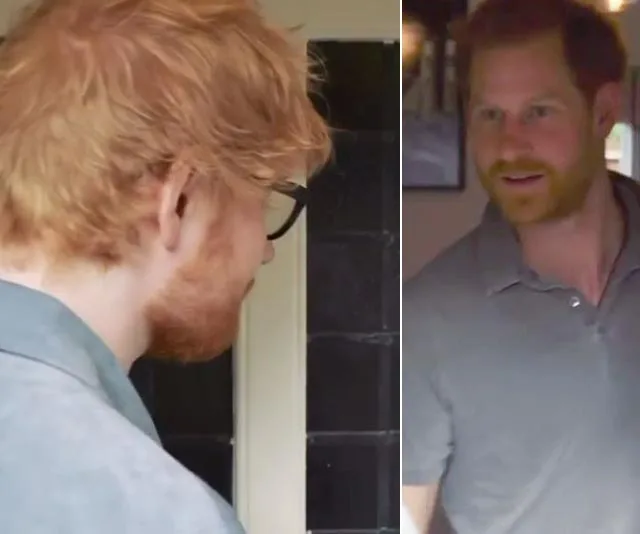 "Two men with red hair, one with glasses, meet indoors, both wearing gray shirts."
