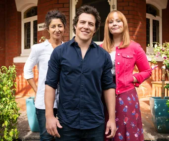 Three characters from "Five Bedrooms" Season 2 smiling in front of a brick house.