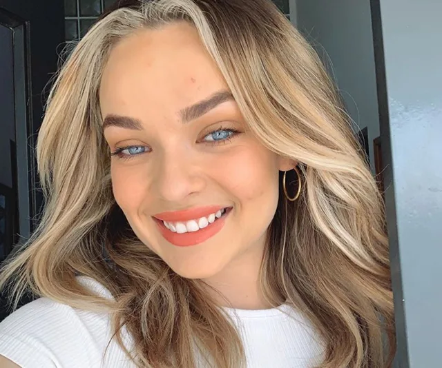 Smiling person with light brown hair and hoop earring, wearing a white shirt.