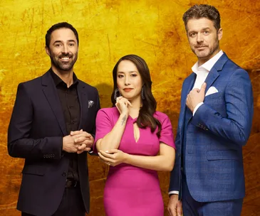 MasterChef judges Andy, Melissa, and Jock pose against a warm yellow background, dressed in formal attire.