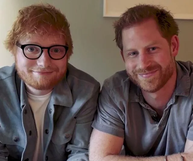 Two smiling men with red hair sitting close together, one wearing glasses, indoors.