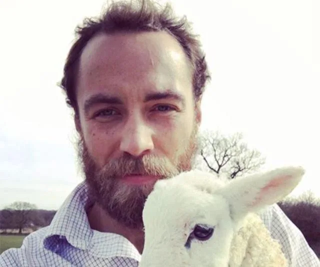 A man with a beard holding a white lamb outdoors under a clear sky.