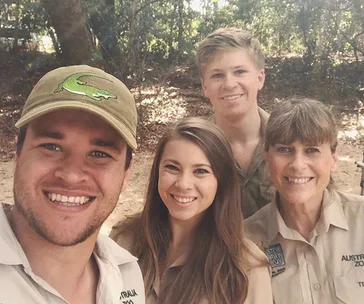 Group of four people smiling outdoors, wearing zoo uniforms in a forested area.
