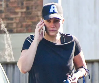 Woman in a black cap and shirt talking on the phone outside.