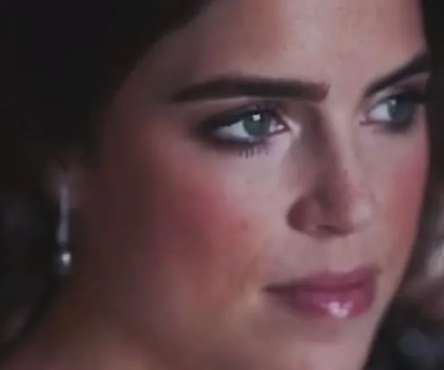 Young woman with subtle makeup, looking thoughtfully to the side, wearing pearl earrings.