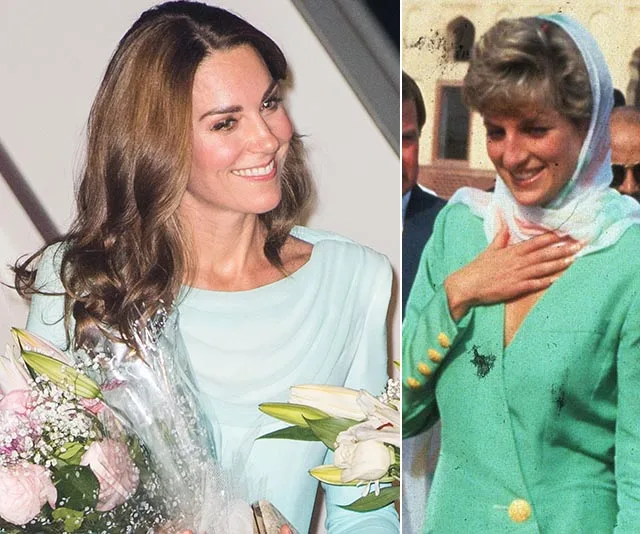 "Two women in similar light green outfits, one holding flowers, both smiling, with a background of people and architecture."
