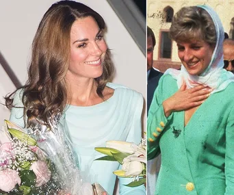 "Two women in similar light green outfits, one holding flowers, both smiling, with a background of people and architecture."