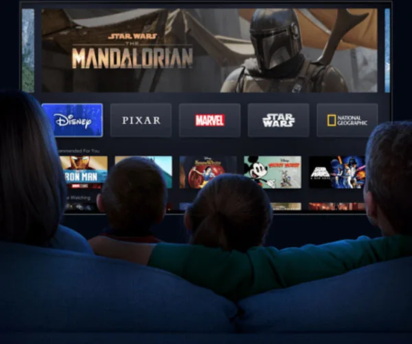 Family watching Disney+ on TV, showing "The Mandalorian" and various Disney categories and recommended shows.