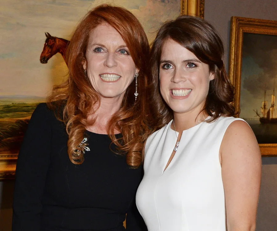Two women smiling in front of a painting; one in black, the other in white, inside an art gallery setting.
