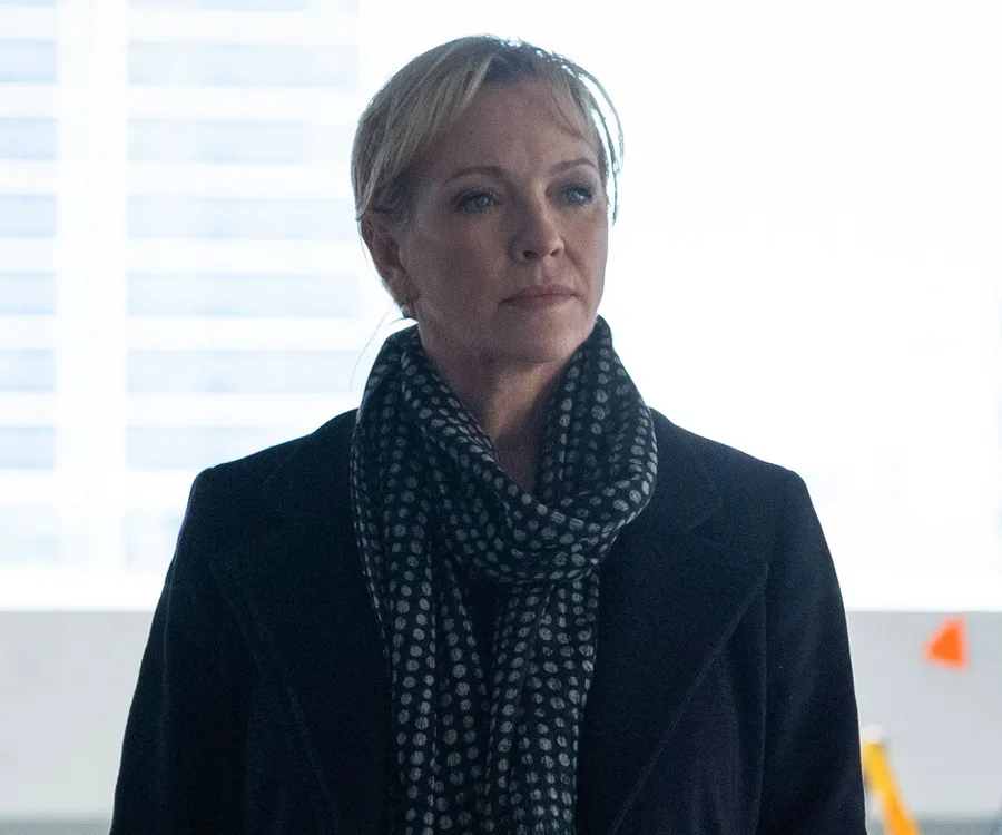 A woman in a polka dot scarf and dark coat stares thoughtfully, background out of focus.