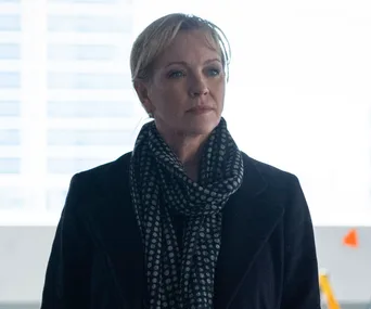 A woman in a polka dot scarf and dark coat stares thoughtfully, background out of focus.