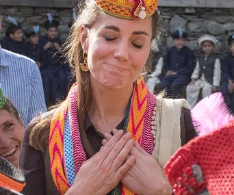 A woman wearing traditional attire and a colorful hat holds her hands to her chest, surrounded by people outdoors.