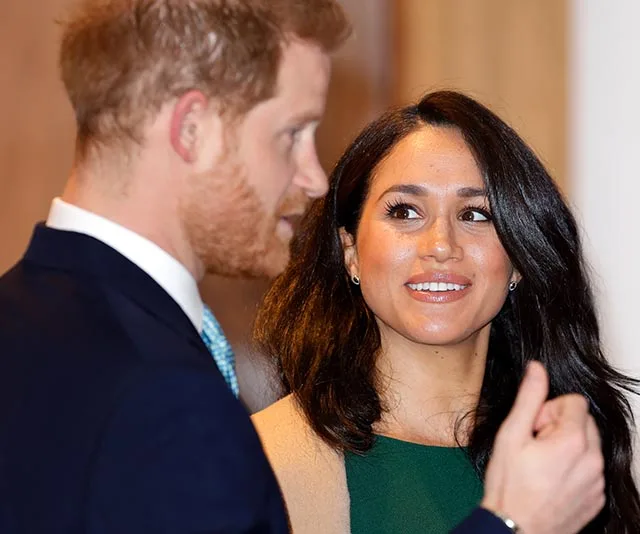 Prince Harry and Meghan Markle smiling and conversing at an event, Meghan wearing a green dress.
