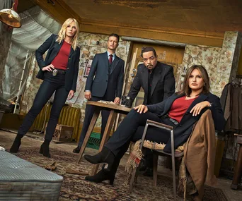 Cast of "Law & Order: SVU" pose in a dimly lit room, wearing formal attire.
