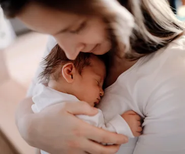Mother gently cradling her sleeping newborn baby close to her chest.