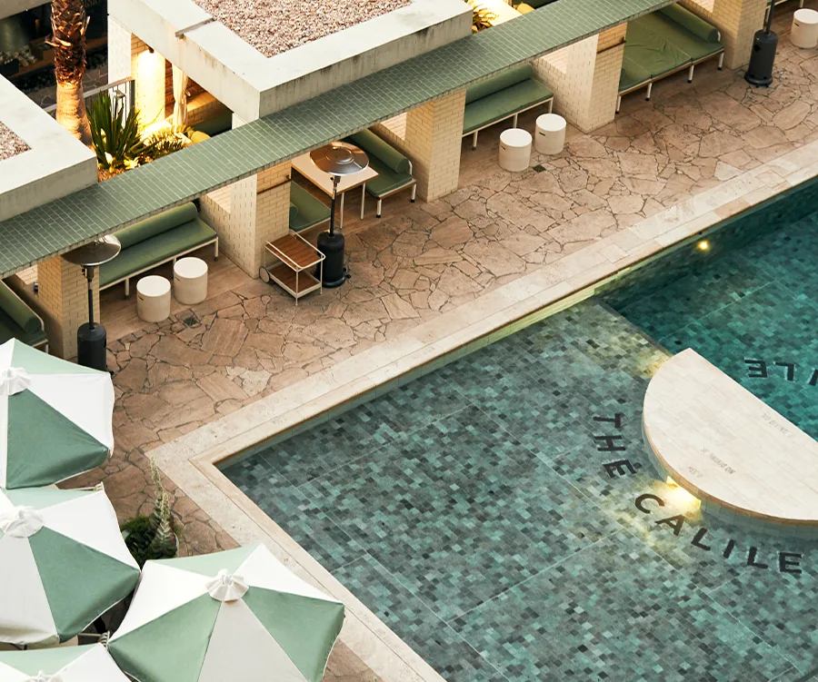 Outdoor pool area with green umbrellas, lounge chairs, and The Calile Hotel branding on the pool tiles.