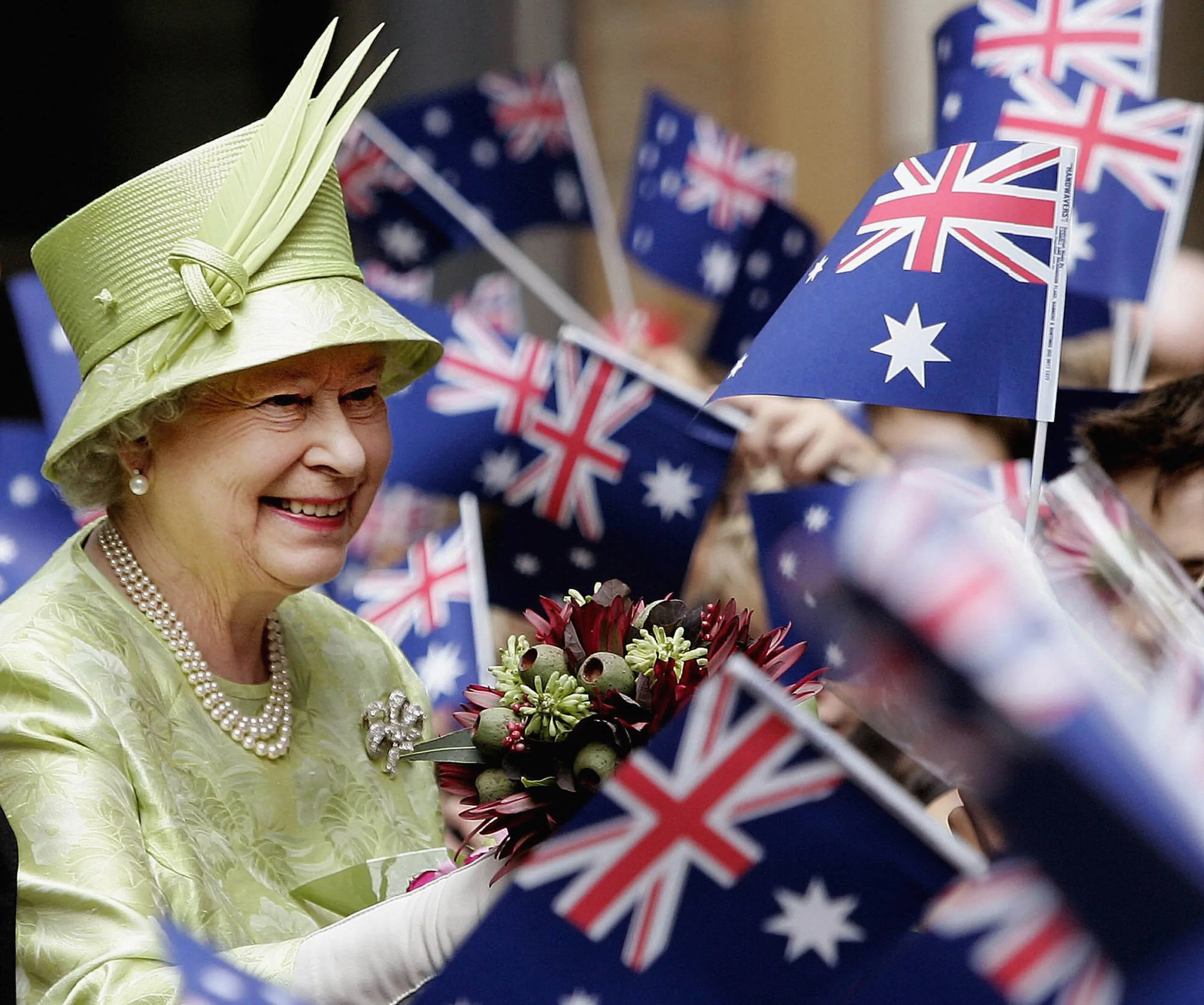 Royal figure in light green attire smiling amidst waving Australian flags.