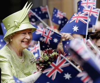 Royal figure in light green attire smiling amidst waving Australian flags.