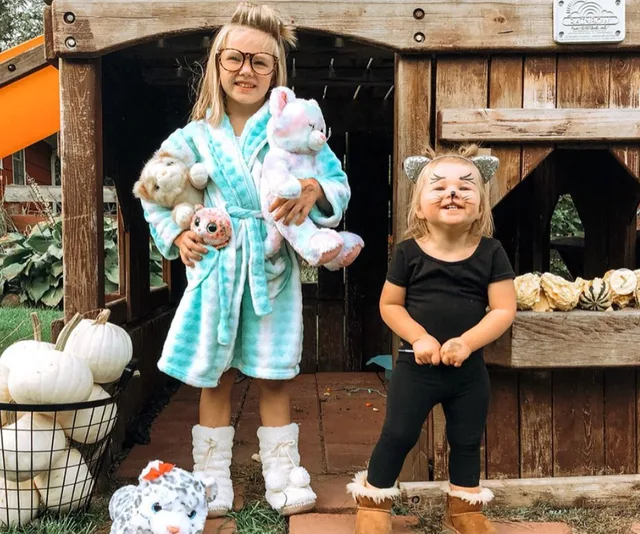 Two kids in Halloween costumes: one in a robe with stuffed animals, the other in cat ears and face paint.
