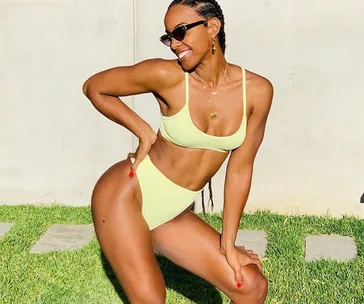 Person posing outdoors in yellow bikini, wearing sunglasses and jewelry, standing on grass.