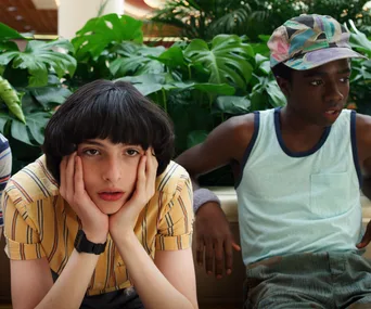 Two teenagers sitting in a mall; one looks bored, hands on face, the other gazes off, wearing a colorful cap.