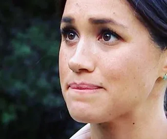 A woman looking emotional outdoors with greenery in the background.