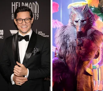 Rob Mills at an event in a tuxedo next to a person in a wolf costume on a colorful stage.