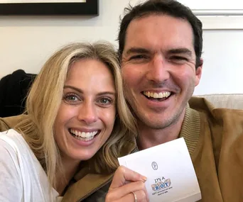 Two people smiling, holding a card that says "It's a Boy."
