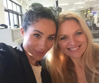 Two women smiling and posing for a selfie at an airport.