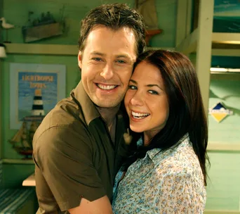 A man and woman smiling and embracing in a cozy room with nautical decor.