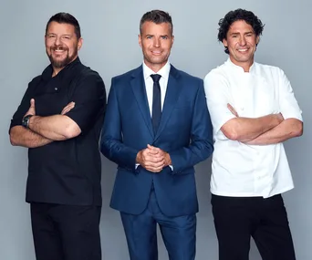 Three men smiling; one in black chef coat, one in blue suit, one in white chef coat, against a light gray background.
