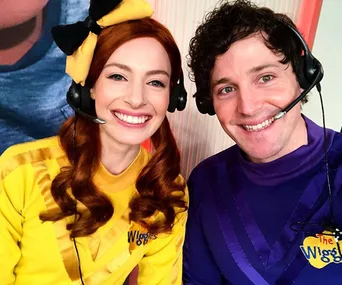 Two members of The Wiggles in yellow and purple outfits, smiling with headsets on.