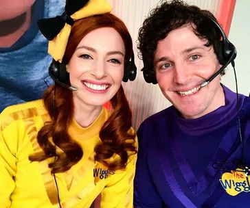 Two members of The Wiggles in yellow and purple outfits, smiling with headsets on.