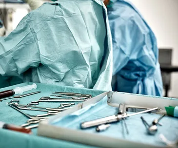 Surgical tools on a tray with medical staff in blue scrubs in the background.