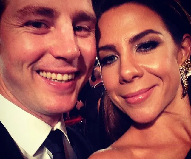 Two people smiling during an event, dressed formally with the woman wearing gold earrings.