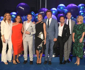 Group photo of people in formal attire, standing on a stage with "Nine" branded balloons in the background.