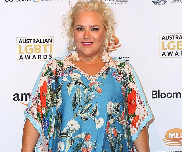 A woman in a colorful floral dress smiles at the Australian LGBTI Awards backdrop.