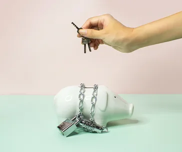 Hand holding keys over a chained and padlocked piggy bank, symbolizing financial restriction or control.