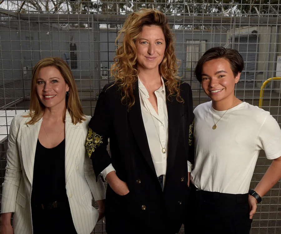 Three individuals standing in front of a wire fence, smiling, with natural outdoor lighting.