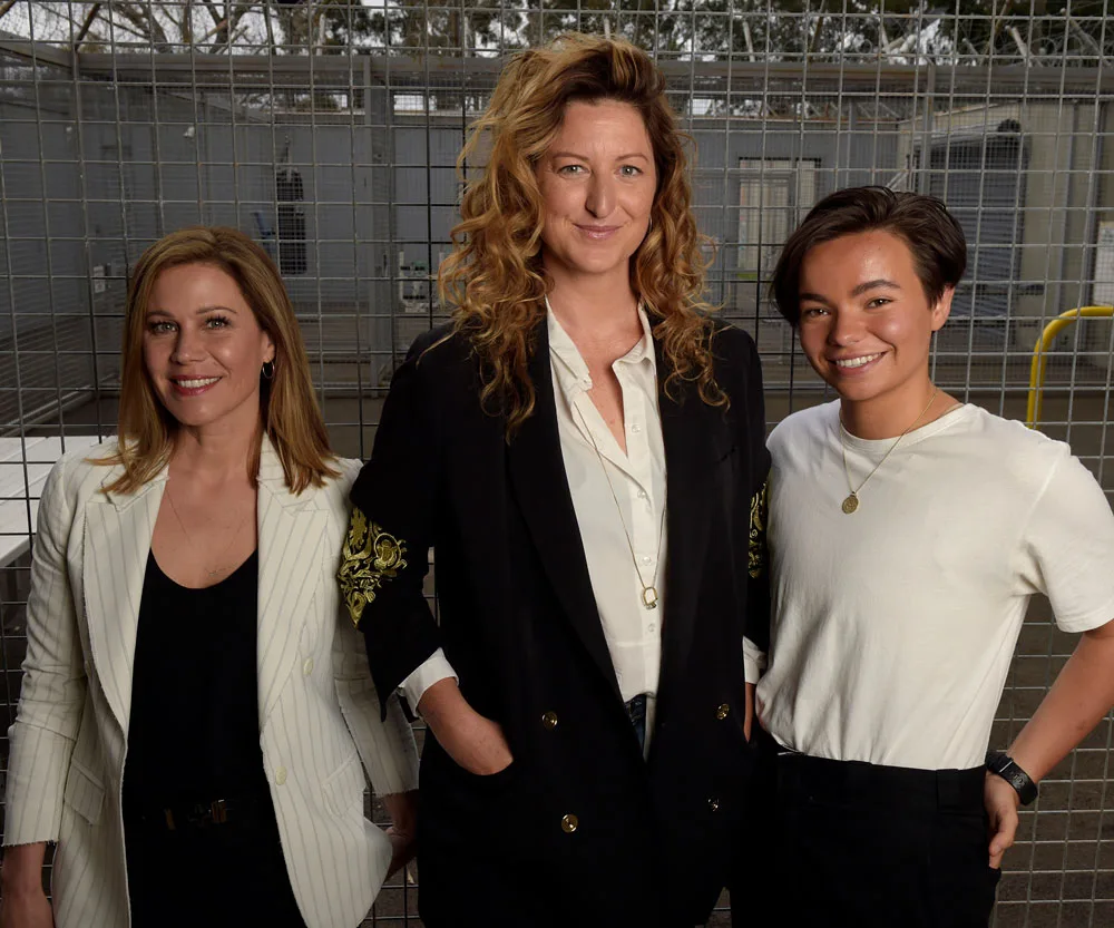 Three individuals standing in front of a wire fence, smiling, with natural outdoor lighting.