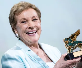 Smiling person holding a gold award statue with a winged lion design.