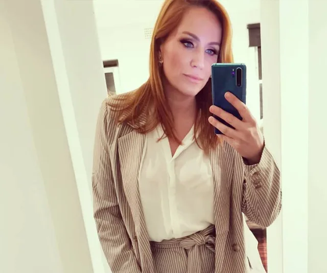 Red-haired woman taking a mirror selfie in a striped suit and white blouse.