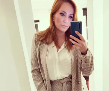Red-haired woman taking a mirror selfie in a striped suit and white blouse.