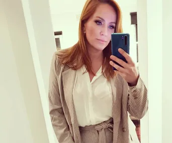 Red-haired woman taking a mirror selfie in a striped suit and white blouse.