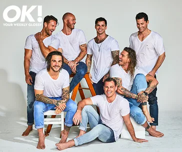 Seven men in white shirts and jeans, smiling and seated or standing against a plain backdrop for a magazine photoshoot.