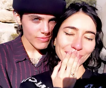 Couple embracing, one with closed eyes, emotional and smiling, wearing a beanie and striped shirt, outdoors.