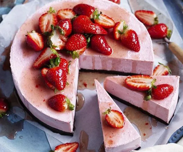 Strawberry vegan cheesecake topped with fresh strawberries, with two slices cut out on a plate.