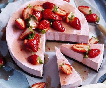 Strawberry vegan cheesecake topped with fresh strawberries, with two slices cut out on a plate.