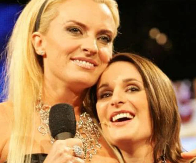Two women smiling, one holding a microphone, likely at an event or show.