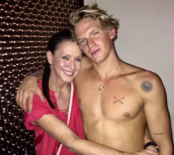 Male with tattoos posing shirtless, smiling woman in red hugs him.